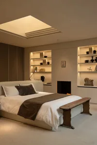 Cozy bedroom with a wooden headboard, brown blanket, and a fireplace, lit by natural light from a skylight