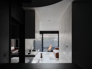 A modern living room with a couch, chair, and dining table, decorated with a vase and illuminated by natural light