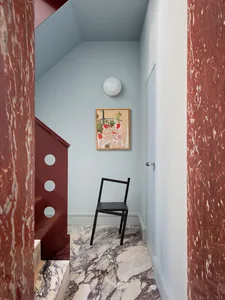 A cozy living area with a black chair as the focal point, surrounded by a blue wall, a red staircase, and a clock on the wall