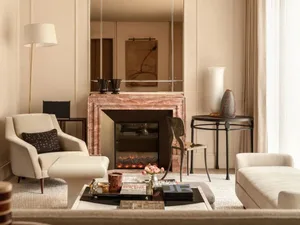Cozy living room with a fireplace, couch, chair, and coffee table, surrounded by neutral colors and minimal decorations, with natural light from the windows