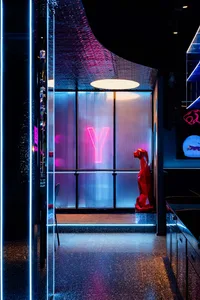 A dimly lit room with a red fire hydrant in the corner, a dining table and chairs in the background, and a modern, minimalist aesthetic