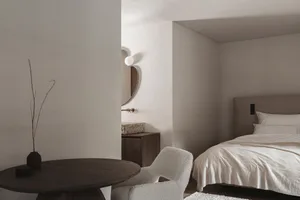 Cozy bedroom with a bed, chair, and table, featuring white furniture and soft warm lighting