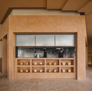A casual restaurant kitchen with a wooden counter, natural light, and two people preparing or enjoying a meal