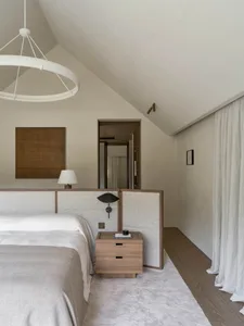 A calm and inviting bedroom with a wooden floor, a bed, a dresser, and a lamp, lit by natural sunlight from a window