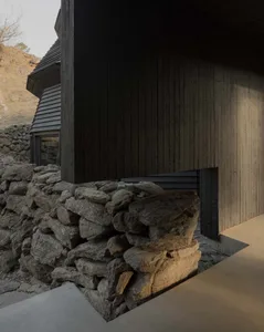 A modern house with a black exterior, stone wall, and black door, bathed in natural sunlight