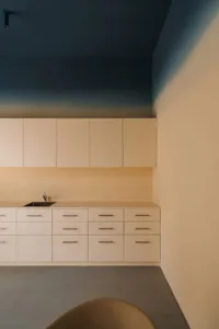 A modern kitchen with white wood cabinets, a marble countertop, a sink, and a cupboard, lit with dim lighting creating a cozy atmosphere