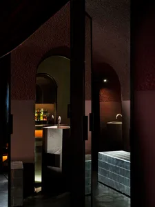 Bathroom with a stone-like appearance, featuring a sink, mirror, and shower, with dim lighting creating a cozy atmosphere