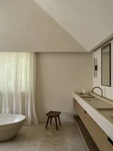 A modern bathroom with a white tub, wooden vanity, and stool, featuring a clean and minimalist design with a well-lit atmosphere