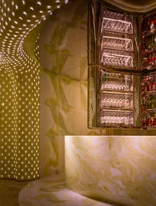 A modern bar with a marble countertop, mirrored surface, and wine glasses, surrounded by bottles and creating a sophisticated atmosphere