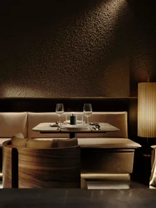 A dimly lit dining room with a wooden table, chairs, and a couch, set with wine glasses and a bottle, creating a cozy and inviting atmosphere