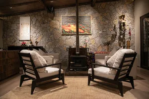 Cozy living room with a stone fireplace, two chairs, and a decorative vase, set in a well-lit space