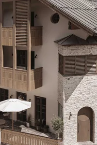 Photograph of a building with a white facade, stone-like appearance, and a balcony and patio area, set in a natural environment