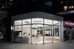 A modern coffee shop with a predominantly white interior, large windows, appliances, and seating areas
