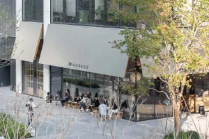 A casual city restaurant with wooden furniture, people seated at tables, and natural sunlight illuminating the scene