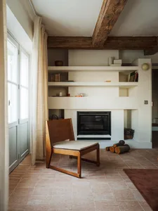 Cozy living room with a fireplace, chair, and bookshelf, featuring wood and stone materials and dim lighting