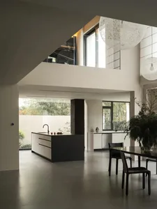 Modern kitchen with a dining area, featuring white walls, grey countertops, and wood flooring, with a potted plant and vase adding a touch of greenery and elegance
