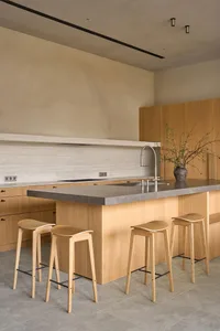 A modern kitchen with wooden cabinets, a marble countertop, and wooden stools, featuring a gray countertop and warm lighting