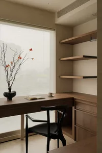 Cozy home office with a wooden desk, a black chair, and a vase with flowers on a natural light-filled room