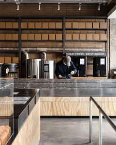A cozy coffee shop with a man behind the counter, surrounded by coffee-making equipment and warm wooden accents, with soft lighting and a welcoming atmosphere
