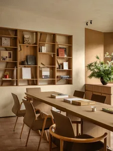 A living room with a wooden table and chairs, surrounded by books and a vase with flowers, on a wooden floor, creating a warm and inviting atmosphere