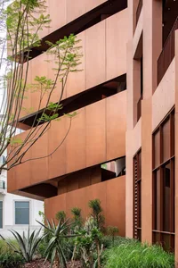 Photograph of a modern building with a brown facade, large window, and balcony, featuring a mix of wood and metal materials in a warm and inviting atmosphere
