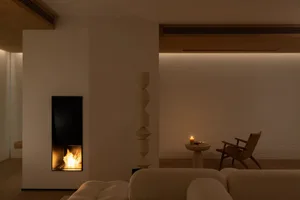Cozy modern living space with a fireplace, couch, chair, and table, well-lit by natural light through a window