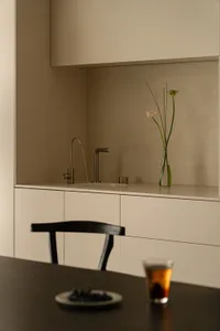 Modern kitchen with a marble counter, metal sink, and a vase with flowers, set against a natural light background