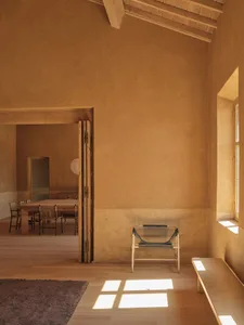 Cozy dining space with a wooden floor, a dining table, chairs, and a bench, surrounded by cement walls and natural light from a window