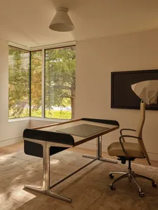 A home office with a black desk and white chair, situated next to a window for natural light, in a clean and organized space