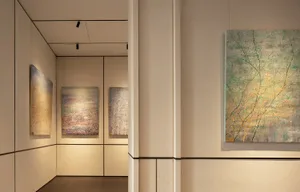 A room with white walls and a doorway, featuring three paintings on the wall and one on the door, in a clean and minimalistic space