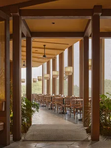 Warm and inviting restaurant interior with wooden furniture, multiple dining tables, and hanging lights