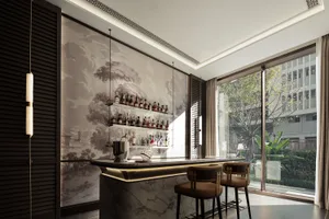 A modern bar with a marble counter, brown chairs, and a large collection of bottles, surrounded by a potted plant in a well-lit setting