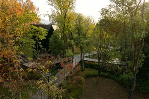 A house with a black exterior and a wooden deck surrounded by trees, with a metal railing along the deck's length