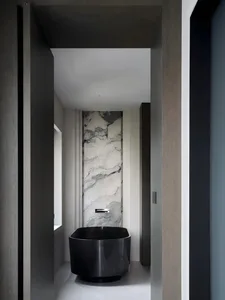 Black and white photograph of a modern bathroom with a black bathtub, toilet, and sink, set against a backdrop of marble walls in a dimly lit space