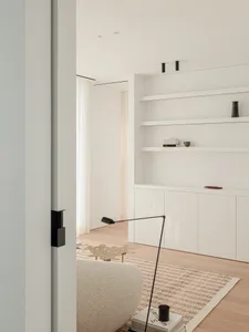 Cozy modern living space with a white color scheme, a couch, a chair, and a bookshelf, well-lit by natural light