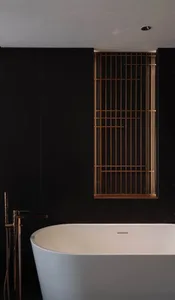 A modern bathroom with a white porcelain bathtub and a black wall, featuring natural light from an open window