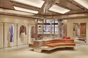 A modern lobby with a large curved wooden bench and a coat rack, surrounded by natural light from a large window