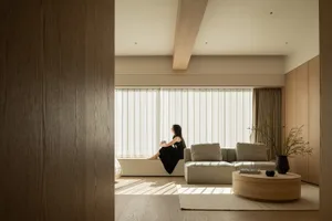 A well-lit living room with a couch, a large window, and a woman sitting on it, enjoying the view