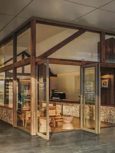 Cozy and inviting interior space with wooden elements, a brick wall, a dining table, and natural light from the glass front