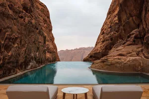 A serene outdoor patio with a pool surrounded by a rock wall, featuring two couches and a dining table