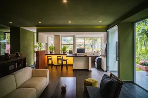 Cozy living room with a green color scheme, featuring a couch, dining table, and kitchen area, with a mix of green and brown colors and a warm atmosphere