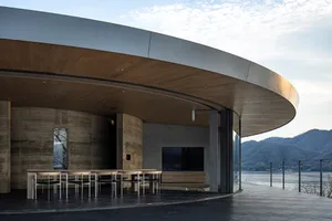 A modern restaurant with a circular seating area featuring a large TV, chairs, and dining tables, surrounded by contemporary materials and well-designed lighting