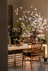 A wooden dining table surrounded by chairs and vases, set against a stone wall in a warm and inviting room