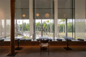 A restaurant with tables and chairs near a large window offering a view of the outdoors, well-lit with natural light and a mix of wood and metal furniture