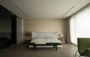 A well-lit modern bedroom with a white bed, black frame, and a nightstand with a vase on top, set against a clean background