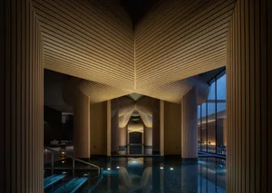 A large modern building with a central swimming pool, surrounded by a spacious area with a warm and inviting wooden design, well-lit by natural light from the windows