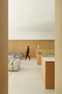 A woman walks through a well-lit living room with a wooden floor, a couch, a chair, and a dining table