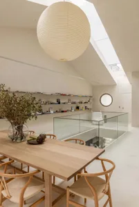 A modern living room with a glass wall, wooden dining table, and cozy atmosphere, decorated with books and potted plants