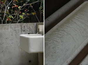 A modern bathroom and staircase with a white porcelain sink, metal faucet, and concrete staircase with metal railing in a dimly lit space