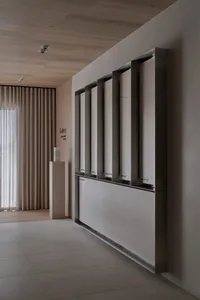 A modern art gallery with a white wall, a sculpture on a pedestal, and natural light from a large window